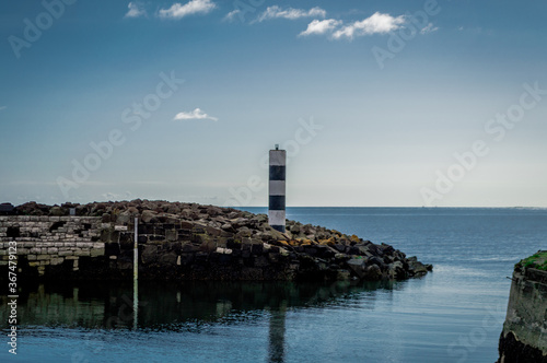 A lonely lighthouse guards the rocky harbor, looking out to sea in Northern Ireland.