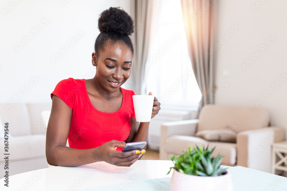 Happy smiling beautiful girl using smartphone device at cozy home , attractive young woman chatting with friends at social network at home and drinking coffee