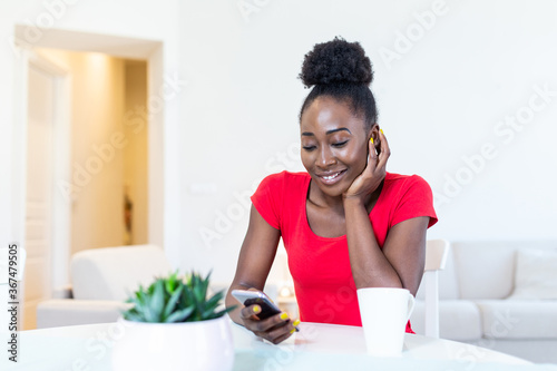 Happy smiling beautiful girl using smartphone device at cozy home , attractive young woman chatting with friends at social network at home and drinking coffee