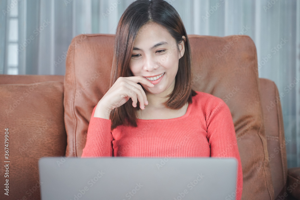 Fototapeta premium Happy asian woman with puppy at home and relaxing with laptop computer on the sofa in the living room. stay at home for coronavirus prevention campaign.Working from home and Online shopping concept.