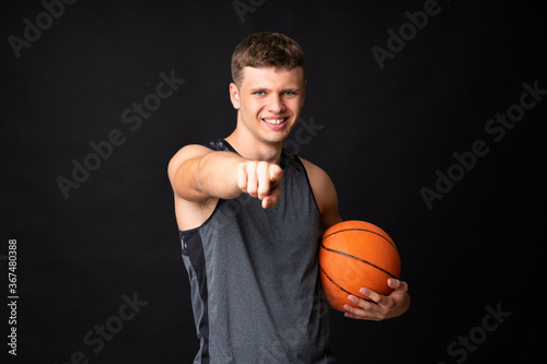 Handsome young man playing basketball over isolated black wall
