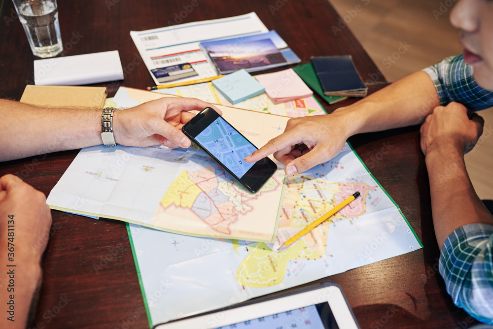 Young people planning trip, they are checking paper maps and online application on smartphone Young people planning trip, they are checking paper maps and online application on smartphone