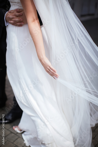 The groom in a black suit embraces the bride in a white dress who straightens the veil. Prepare for a meeting and a stylish luxury wedding ceremony.