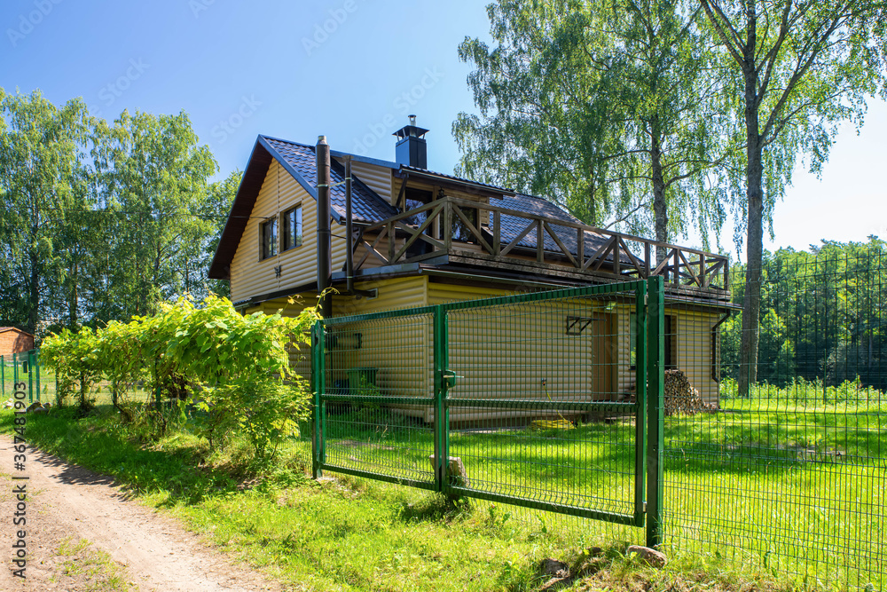 Rural dusty road near the countryside private house with wooden terrace. Modern exterior. Woodpile near the wall.