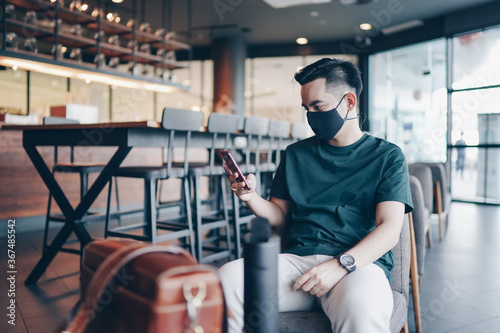 Attractive asian businessman with mask using smartphone at cafe. Drinking coffee and surfing the internet and read news. social distancing concept.