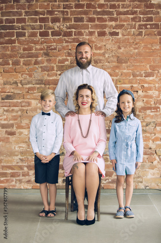 Classic. Happy family traditional portrait, old-fashioned. Cheerful parents and kids in official styled attire on dark vintage background. Concept of human emotions, memories, togetherness, fun.