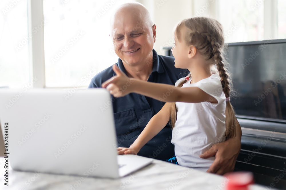 Portrait of grandfather and granddaughter doing homework with laptop.
