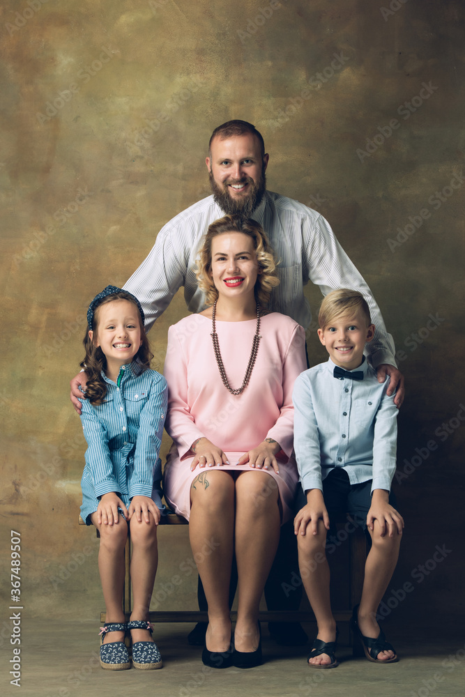 History. Happy family traditional portrait, old-fashioned. Cheerful parents and kids in official styled attire on dark vintage background. Concept of human emotions, memories, togetherness, fun. History. Happy family traditional portrait, old-fashioned. Cheerful parents and kids in official styled attire on dark vintage background. Concept of human emotions, memories, togetherness, fun.
