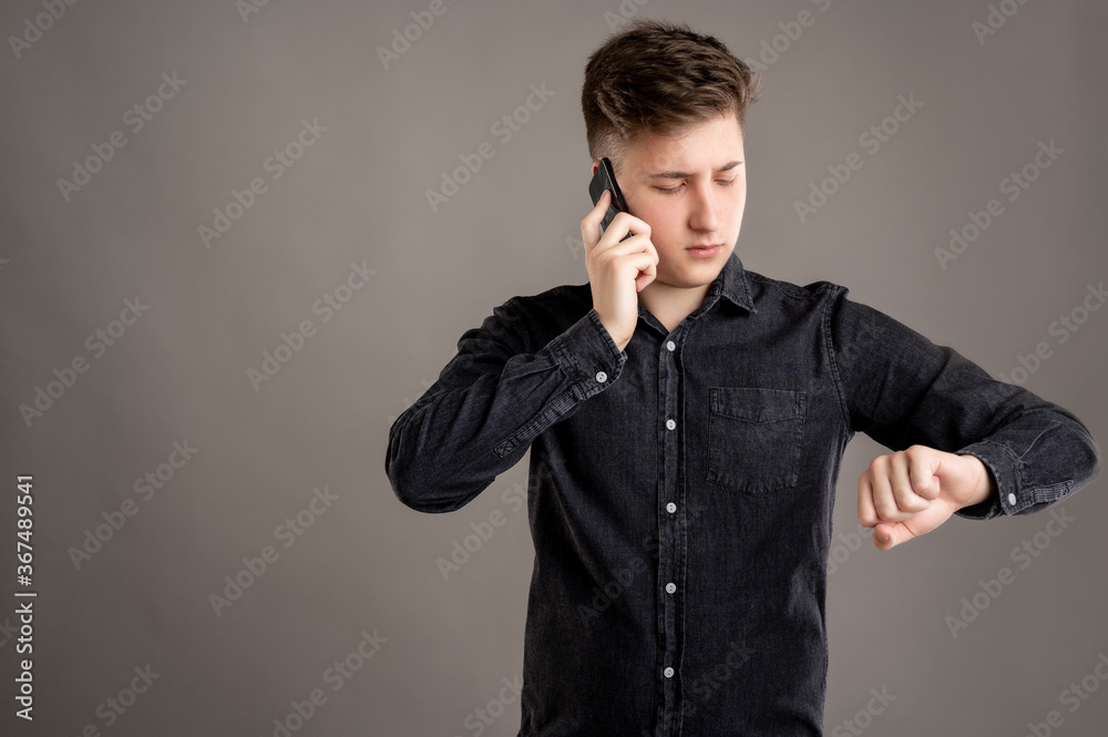 Portrait of serious stylish attractive man dressed with a casual black shirt talking on the phone and looking his watch Portrait of serious stylish attractive man dressed with a casual black shirt talking on the phone and looking his watch