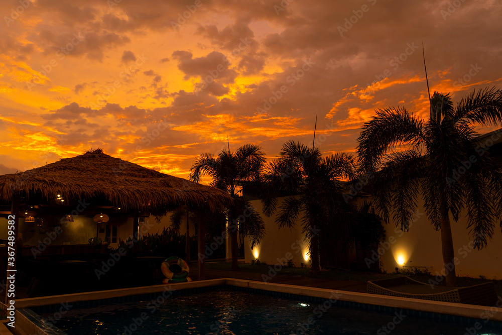 Beautiful orange fiery sunset in the tropics. Street canopy from hay, next to the pool and overlooking the rice field.