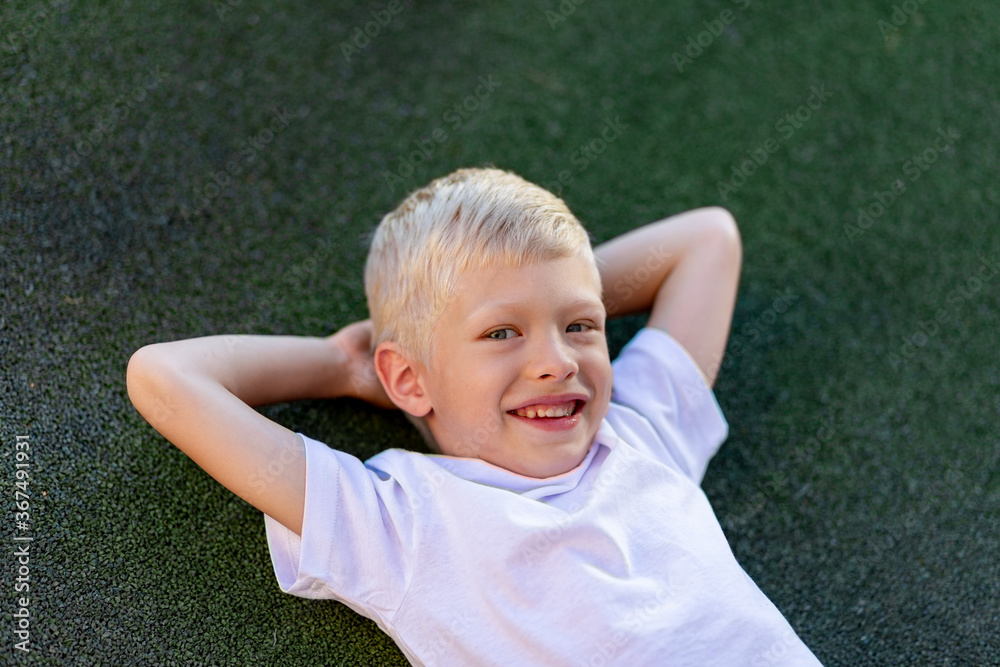 portrait of a blond boy in a sports uniform lying on the football field, sports section. Training of children, children's leisure portrait of a blond boy in a sports uniform lying on the football field, sports section. Training of children, children's leisure