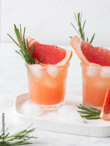 Grapefruit lemonade. Two cold wet drinking glasses with fresh grapefruit nonalcohol beverage. Ice, rosemary.