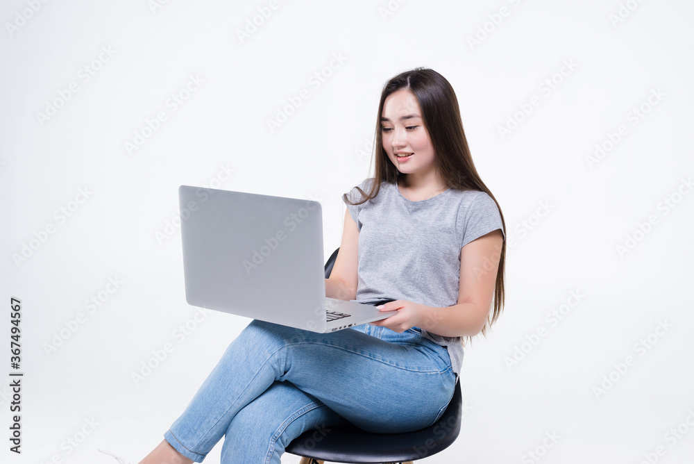 Asian businesswoman talking on the phone and looking at a laptop while sitting on a chair isolated on white background Asian businesswoman talking on the phone and looking at a laptop while sitting on a chair isolated on white background