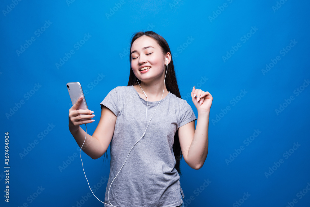 Φωτογραφία Cheerful young asian woman in headphones listening to music and dancing over blu