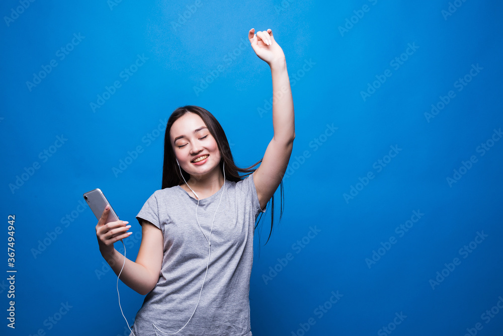 Φωτογραφία Cheerful young asian woman in headphones listening to music and dancing over blu
