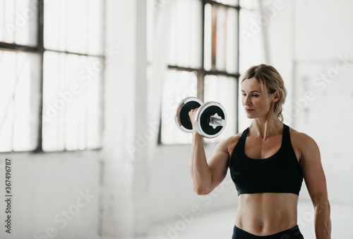 Strength training in studio. Athletic woman in sport bra engaged with dumbbells