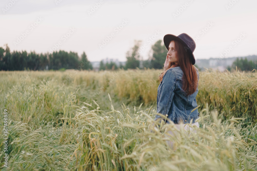 Beautiful young girl in a denim jacket in a green field of rye at sunset