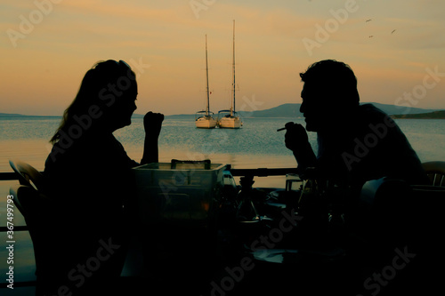 A couple having dinner in sunset time at sea side with sailboats and sea view.