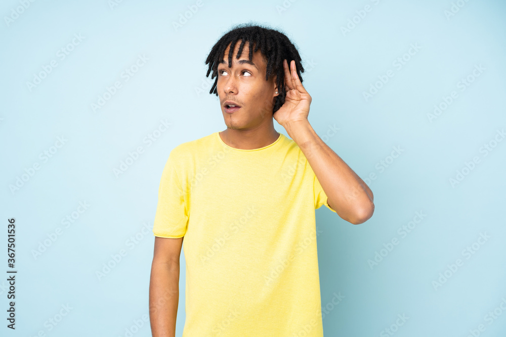 Young african american man isolated on blue background listening to something by putting hand on the ear Young african american man isolated on blue background listening to something by putting hand on the ear