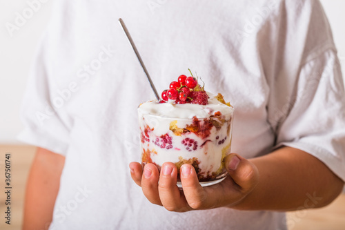 Layered trifle dessert with sponge cake, whipped cream and raspberries in child hands photo