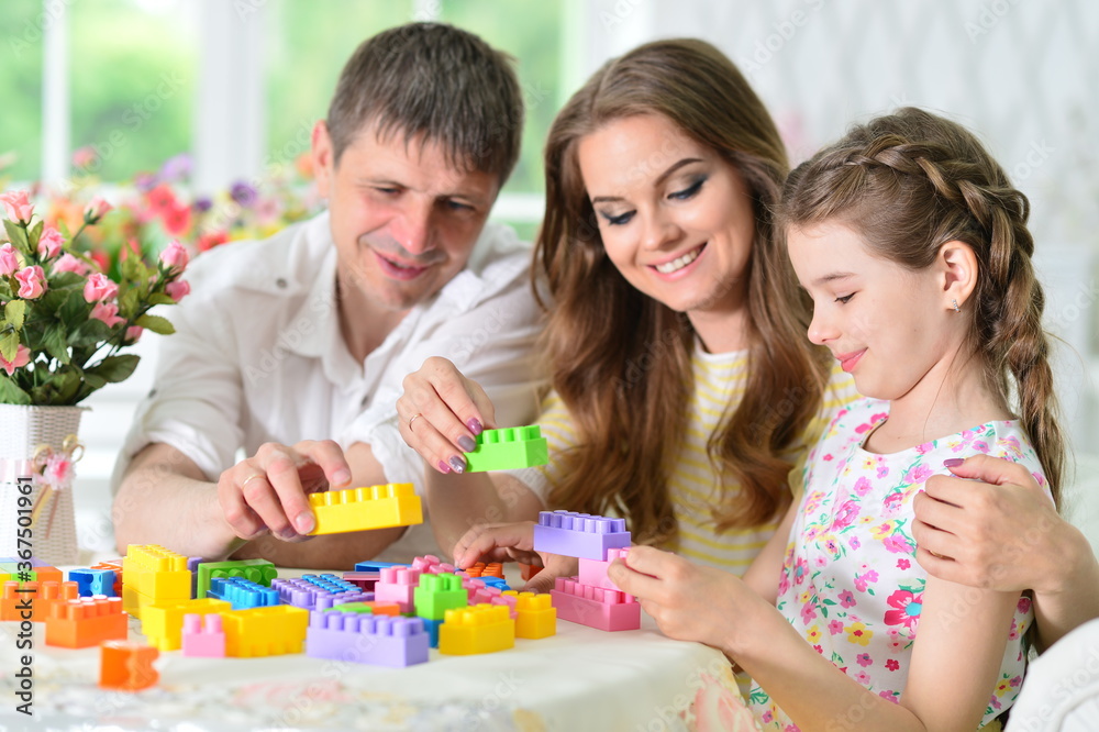 Girl with mother and father playing with colorful plastic blocks