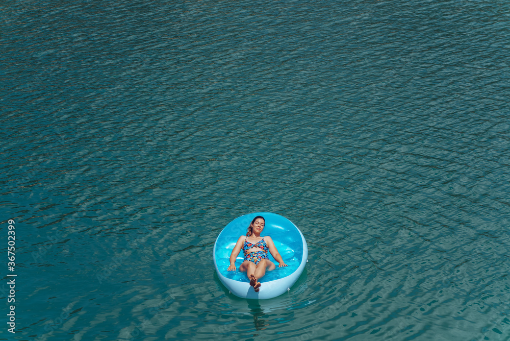 Fototapeta premium Young woman relaxing at the beach while sunbathing on a floating mattress