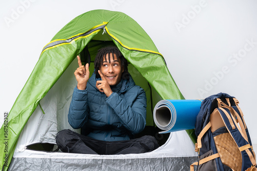 Young african american man inside a camping green tent pointing with the index finger a great idea
