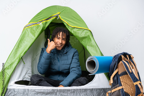 Young african american man inside a camping green tent making phone gesture. Call me back sign