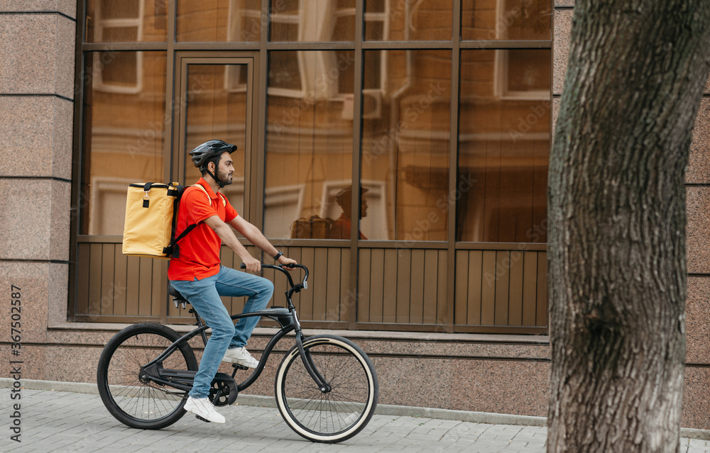 Fast delivery in city. Young man with helmet and delivery backpack rides bicycle