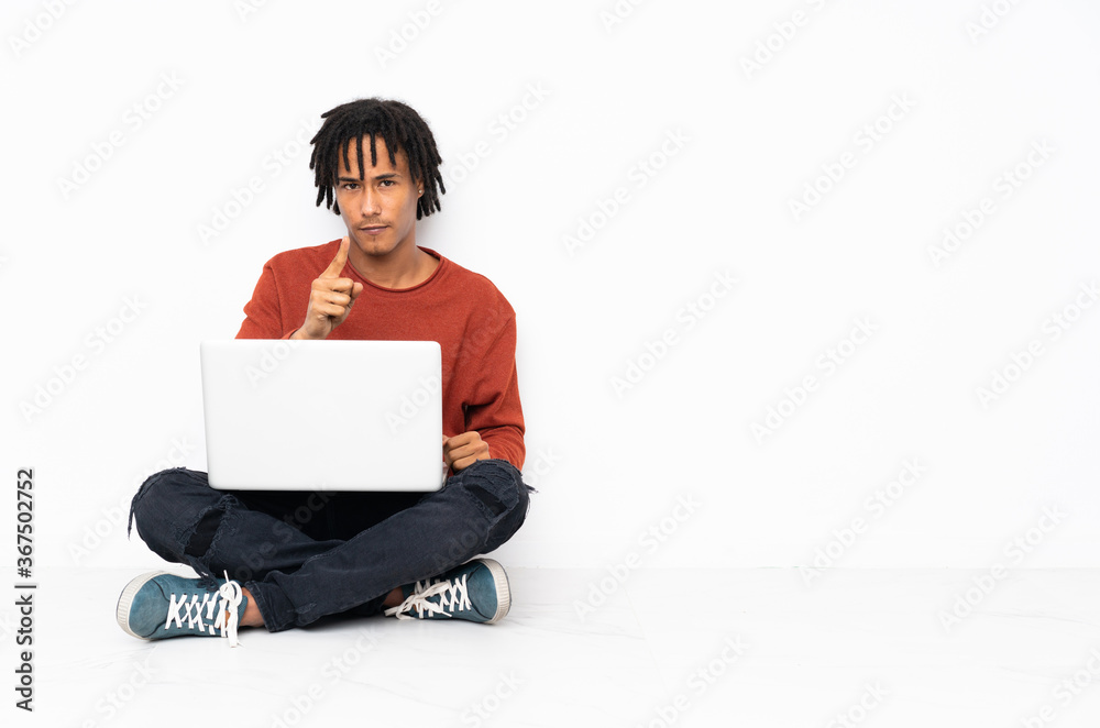 Young african american man sitting on the floor and working with his laptop frustrated and pointing to the front Young african american man sitting on the floor and working with his laptop frustrated and pointing to the front