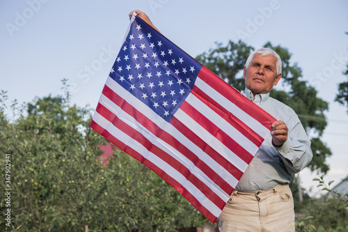Patriotic senior man celebrates usa independence day on 4th of July with a national flag in his hands. Constitution and Citizenship Day. National Grandparents day