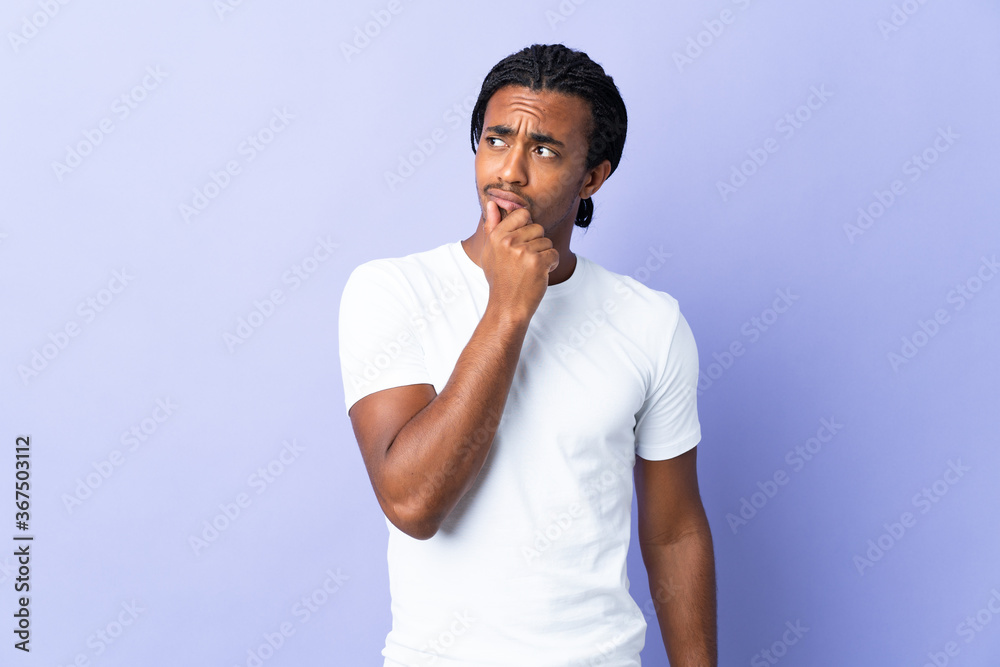 Young African American man with braids man isolated on purple background having doubts Young African American man with braids man isolated on purple background having doubts
