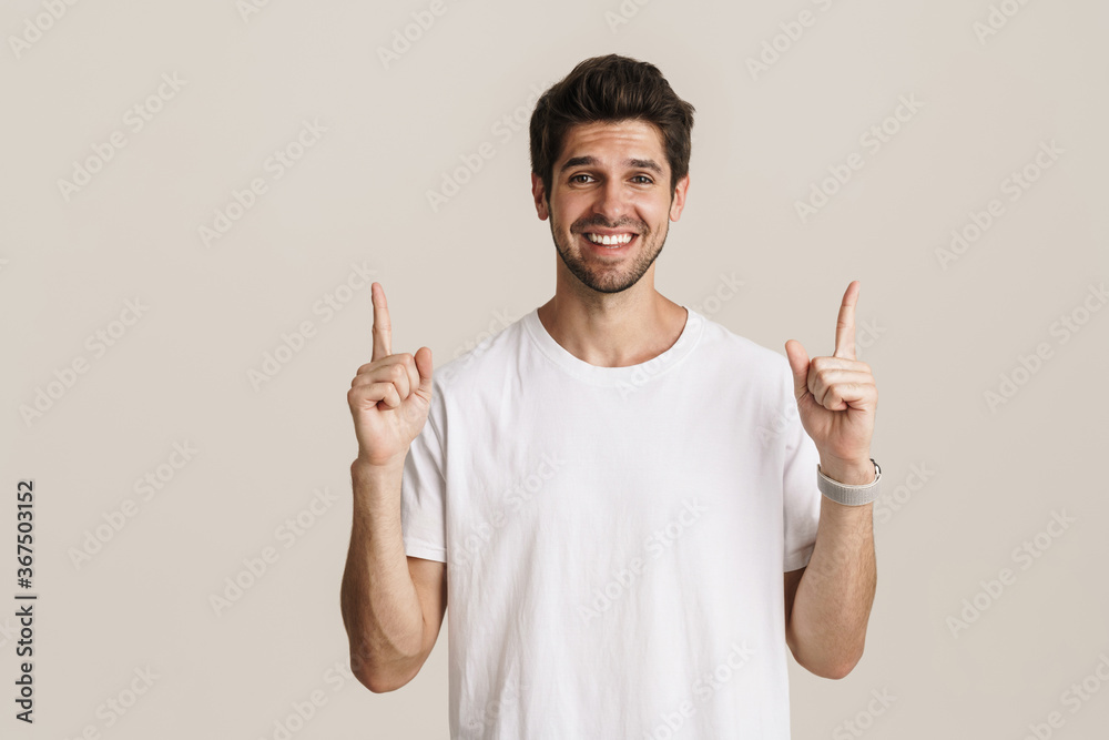 Image of joyful young man smiling and pointing fingers upward Image of joyful young man smiling and pointing fingers upward