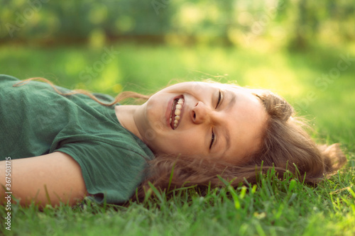 Happy laughing fun casual kid girl lying on the grass on nature summer background. Closeup