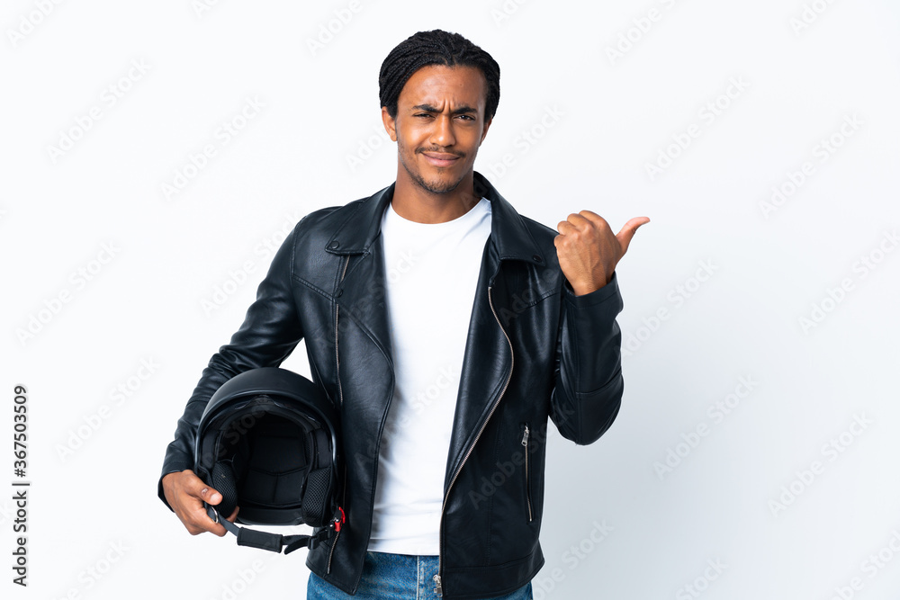 African American man with braids holding a motorcycle helmet isolated on white background pointing to the side to present a product African American man with braids holding a motorcycle helmet isolated on white background pointing to the side to present a product