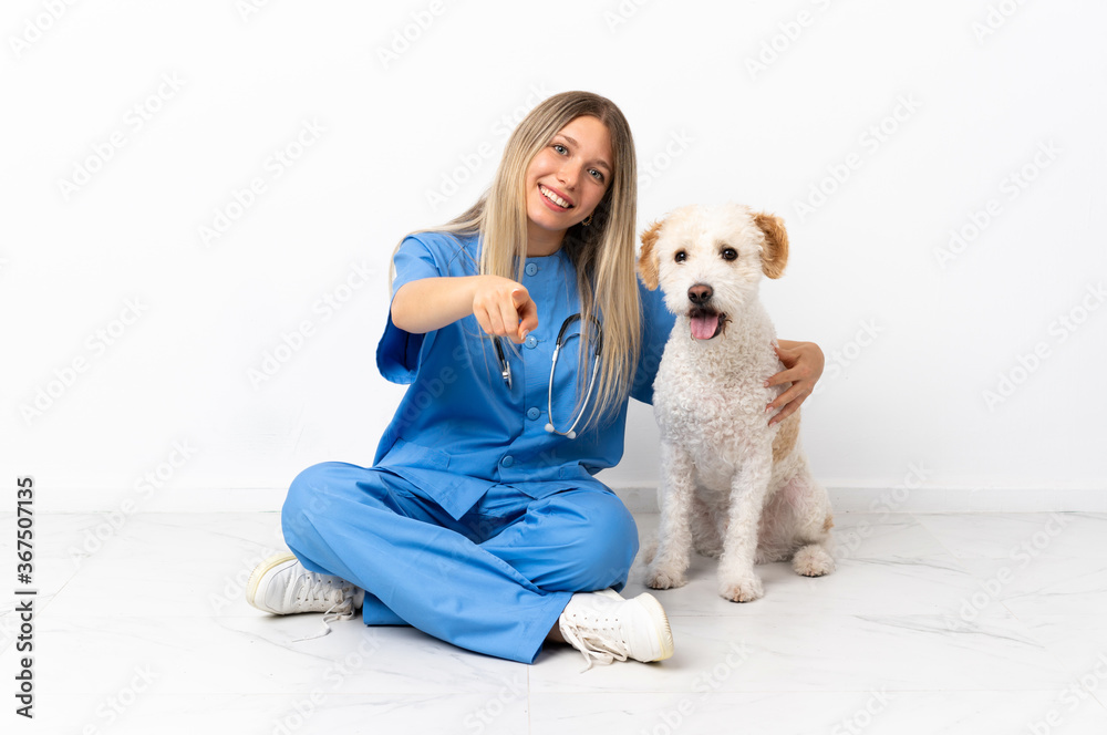 Young veterinarian woman with dog sitting on the floor pointing front with happy expression Young veterinarian woman with dog sitting on the floor pointing front with happy expression