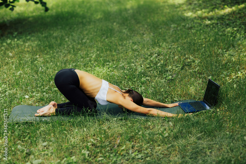 Young attractive woman doing yoga exercise in park, she doing Kurmasana Half Tortoise Pose. Working out wearing sportswear white bra and black pants. photo