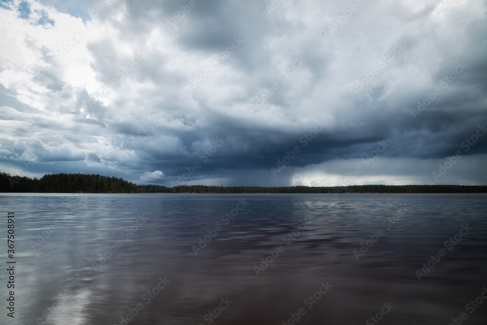 Rain clouds on the horizon over a lake and forest. Dark lake before storm.