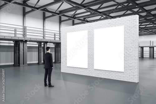 Businessman standing in showroom with exhibition brick stand with two blank posters.