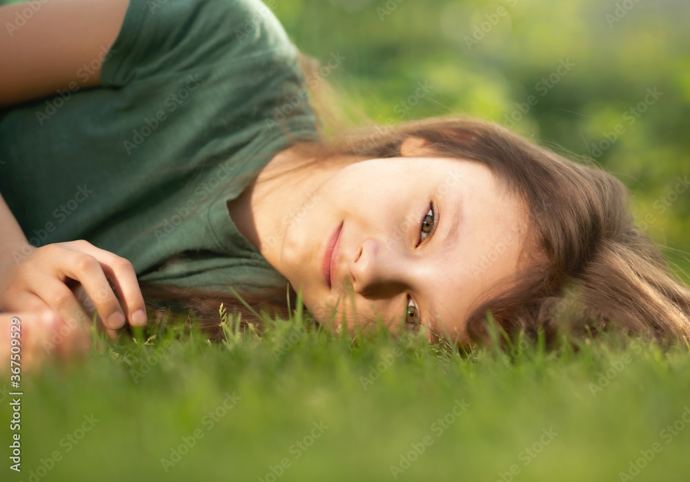 Happy smiling calm casual kid girl lying on the grass on nature summer background. Closeup Happy smiling calm casual kid girl lying on the grass on nature summer background. Closeup