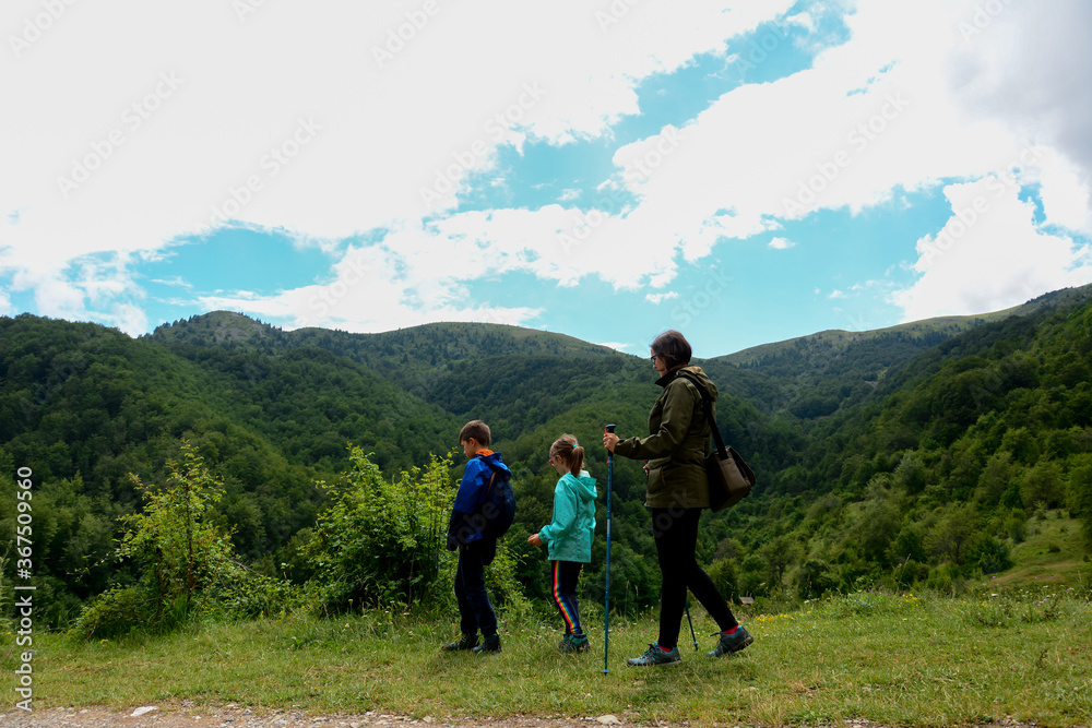 Mother and two children enjoying a walk in the mountain trail, side view.