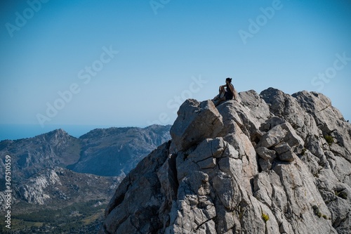 A man sits on a rock during a trekking on a mountain looking at the stunning views of Serra de Tramuntana (Mallorca, Spain)