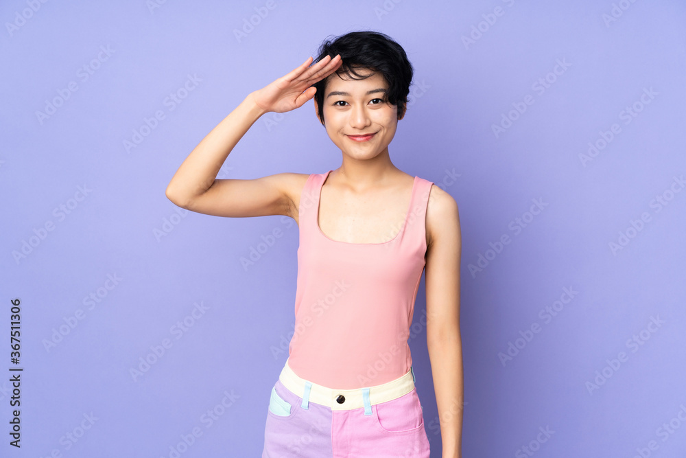 Young Vietnamese woman with short hair over isolated purple background saluting with hand with happy expression Young Vietnamese woman with short hair over isolated purple background saluting with hand with happy expression