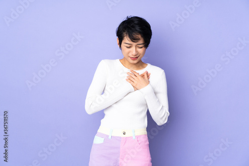 Young Vietnamese woman with short hair over isolated purple background having a pain in the heart