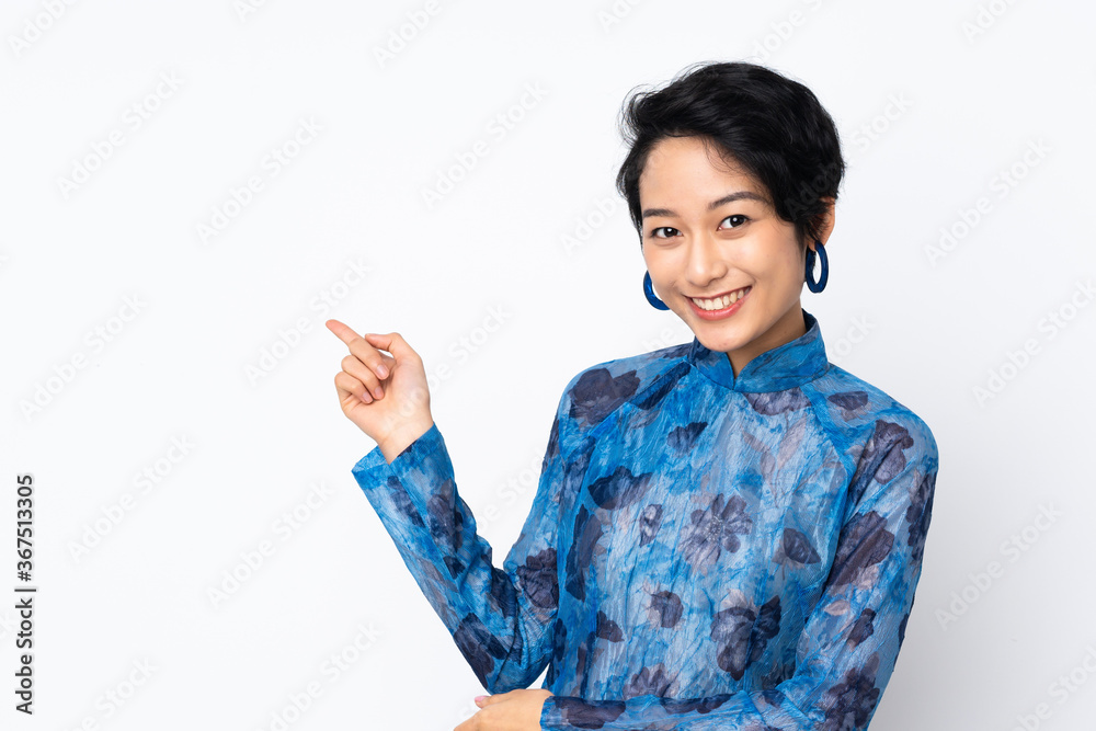 Young Vietnamese woman with short hair wearing a traditional dress over isolated white background pointing finger to the side Young Vietnamese woman with short hair wearing a traditional dress over isolated white background pointing finger to the side