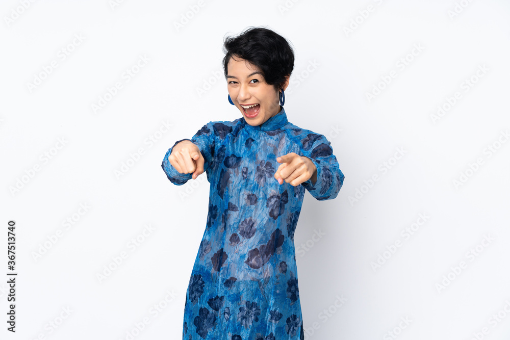 Young Vietnamese woman with short hair wearing a traditional dress over isolated white background surprised and pointing front Young Vietnamese woman with short hair wearing a traditional dress over isolated white background surprised and pointing front
