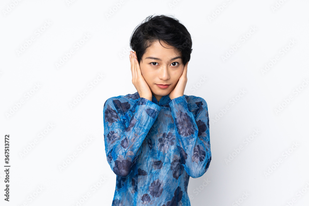 Young Vietnamese woman with short hair wearing a traditional dress over isolated white background frustrated and covering ears Young Vietnamese woman with short hair wearing a traditional dress over isolated white background frustrated and covering ears