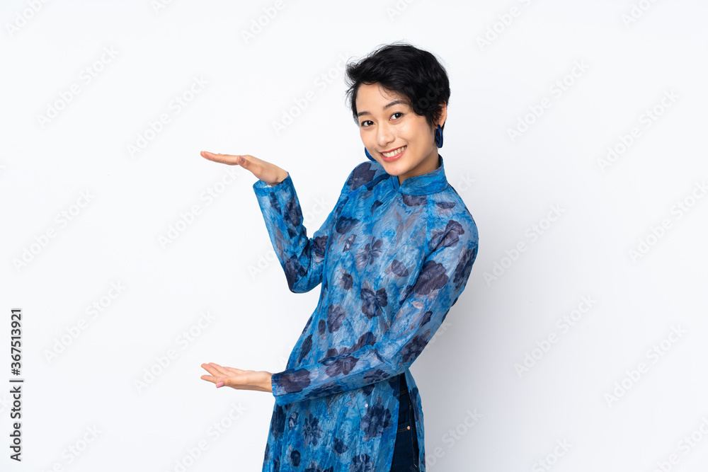 Young Vietnamese woman with short hair wearing a traditional dress over isolated white background holding copyspace to insert an ad Young Vietnamese woman with short hair wearing a traditional dress over isolated white background holding copyspace to insert an ad