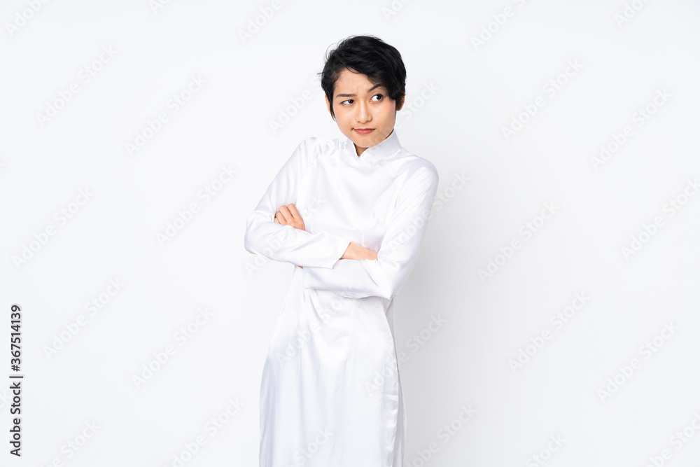 Young Vietnamese woman with short hair wearing a traditional dress over isolated white background making doubts gesture while lifting the shoulders Young Vietnamese woman with short hair wearing a traditional dress over isolated white background making doubts gesture while lifting the shoulders