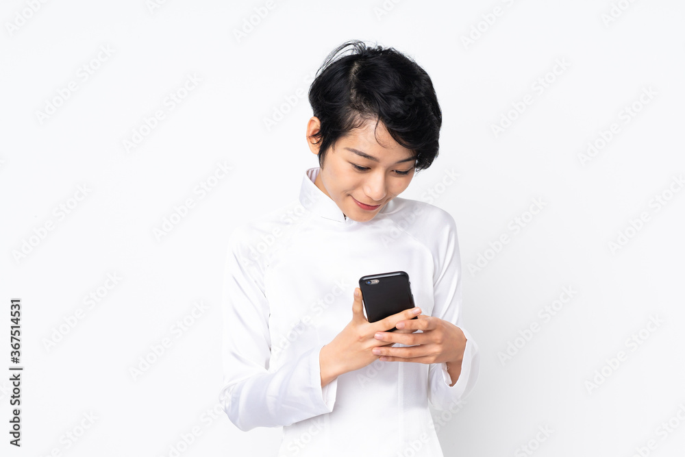 Young Vietnamese woman with short hair wearing a traditional dress over isolated white background sending a message with the mobile Young Vietnamese woman with short hair wearing a traditional dress over isolated white background sending a message with the mobile